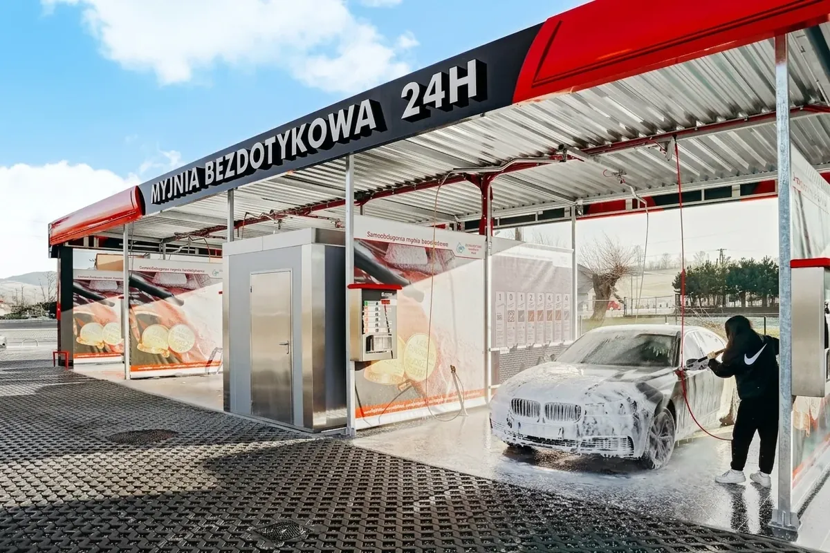 Samoobsługowa myjnia bezdotykowa czynna 24h. Klientka myje pianą samochód na stanowisku.